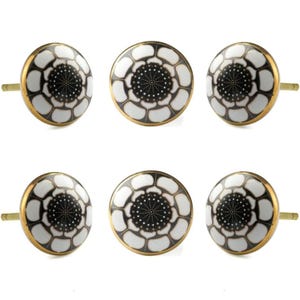 Op de afbeelding: Zes ronde kastknoppen met een bloemmotief. Elke knop heeft een wit en zwart bloemmotief, een goudkleurige rand en een goudkleurige steel. De knoppen zijn waarschijnlijk gemaakt van keramiek en geschikt voor meubels.