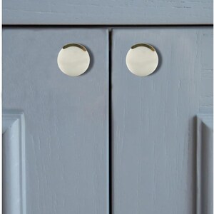 May include: Close-up of a light blue cabinet with two white and gold cabinet knobs. The knobs are round with a gold trim and a white center. The cabinet doors have a recessed panel design.
