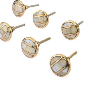 May include: Set of six decorative cabinet knobs. Each knob features a round, gold-colored metal base with a white and cream-colored inlay. The knobs have a threaded post for easy installation. Ideal for adding a touch of elegance to furniture.