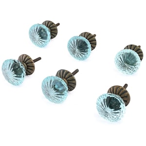 May include: A set of six round cabinet knobs featuring translucent light blue glass with a radial ribbed pattern. Each knob has a dark bronze-toned metal base with a fluted design and a threaded metal screw extending from the back for installation.