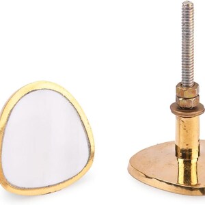 Könnte beinhalten: Zwei dekorative Schrankknöpfe. Einer hat eine weiße, dreieckige Front mit goldfarbenem Rand. Der andere hat einen goldfarbenen Sockel und einen Gewindebolzen zur Montage. Montagematerial ist enthalten. Geeignet für Möbel.