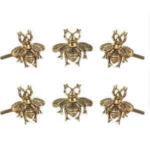 Peut inclure: Six boutons de meuble dorés en forme d'abeille. Chaque bouton présente un motif d'abeille détaillé avec des ailes et un corps texturé. Les boutons ont une vis pour une installation facile et conviennent aux meubles ou à la décoration.