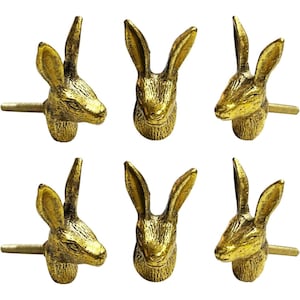 May include: Six gold-coloured cabinet knobs shaped like rabbit heads. Each knob features a detailed rabbit face with long ears and a screw for attachment. The knobs are made of a metallic material and are designed for furniture.