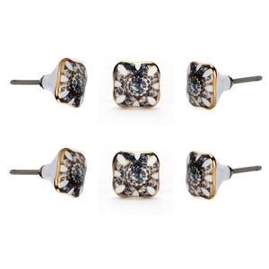 May include: Six decorative square cabinet knobs. Each knob features a white base with a gold trim and a black and white floral design. The knobs have a silver screw for easy installation.