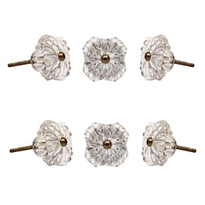 Könnte beinhalten: Sechs transparente Glasschrankknöpfe mit einem facettierten, blütenartigen Design. Jeder Knopf hat eine messingfarbene Mitte und einen Gewindestift zur Montage. Die Knöpfe sind vor einem weißen Hintergrund angeordnet.