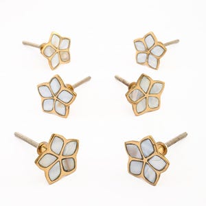 May include: Six decorative flower-shaped cabinet knobs. Each knob features a gold-colored metal frame with a five-petal design. The petals are filled with a pearlescent white material, and each knob has a threaded metal stem for installation.
