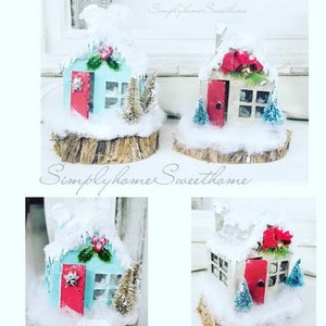 May include: Handmade Christmas village houses with snow-covered roofs, red doors, and miniature trees. The houses are set on wooden bases and decorated with festive accents. The text "Simplyhome Sweet home" is visible.