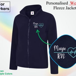 Può includere: Giacca in pile blu navy con cerniera intera e collo alto. La giacca presenta il testo "Maizie RN" con un grafico a forma di battito cardiaco. Il testo "For Workers" è in un riquadro bianco in alto a sinistra.