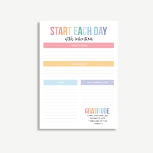 May include: A white notepad with the text "START EACH DAY with intention" in colorful letters. The notepad includes sections for goals, affirmations, tasks, and gratitude, with the phrase "GRATITUDE turns the smallest moments into treasures of the heart."