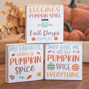 May include: Three white wooden blocks with fall-themed text and graphics. The blocks read "LEGGINGS PUMPKIN SPICE", "MY FAVORITE color is PUMPKIN SPICE", and "JUST GIVE ME all the PUMPKIN SPICE EVERYTHING".