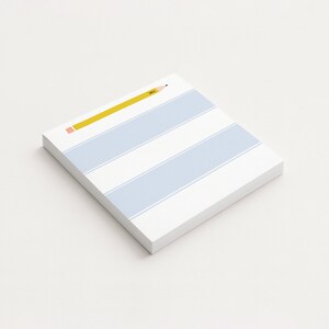 May include: A white notepad with light blue stripes and a yellow pencil illustration. The pencil is positioned diagonally across the top of the notepad. The notepad is rectangular and appears to be made of paper.