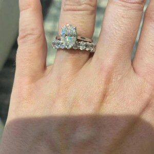 May include: Close-up of two rings on a finger. The top ring has a large, oval-cut diamond. The second ring is a band with multiple smaller diamonds. Both rings are set in silver or white metal.