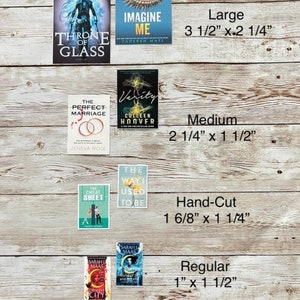May include: A collection of book covers in different sizes, including "Throne of Glass" by Sarah J. Maas, "Imagine Me" by Tahereh Mafi, "The Perfect Marriage" by Geneva Rose, "Verity" by Colleen Hoover, "The Cheat Sheet" by Sarah Adams, "The Way I Used to Be" by Amber Smith, and "Crescent City" by Sarah J. Maas. The covers are arranged in a grid pattern on a wooden surface. The sizes of the covers are labeled as "Large", "Medium", "Hand-Cut", and "Regular".