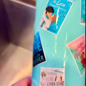 Puede incluir: Un vaso de acero inoxidable turquesa con varias pegatinas de portadas de libros. Las pegatinas presentan t&iacute;tulos como "The Love Hypothesis", "My Killer Vacation" y "Love & Other Words".