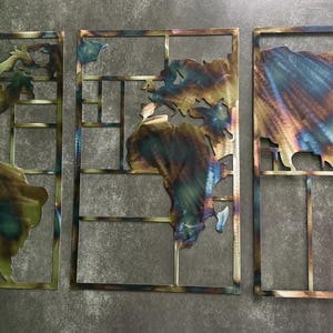 May include: A set of three rectangular metal wall art panels featuring a world map divided into sections. The continents are crafted from heat-treated steel with iridescent blue, gold, and bronze tones, set within a grid-like metal frame.
