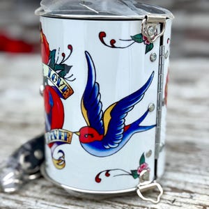 May include: A white ceramic mug with a black handle and the text "But First, Coffee" in a bold, black font. The mug is set against a blurred background, suggesting a cozy setting. The mug appears to be approximately 4 inches tall.
