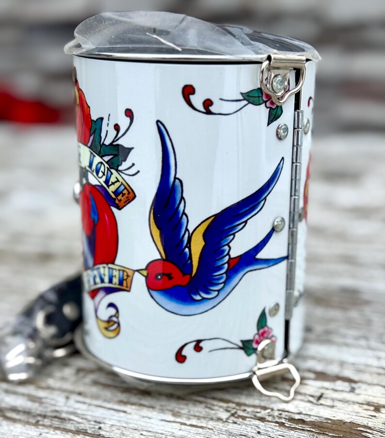 May include: A white ceramic mug with a black handle and the text "But First, Coffee" in a bold, black font. The mug is set against a blurred background, suggesting a cozy setting. The mug appears to be approximately 4 inches tall.
