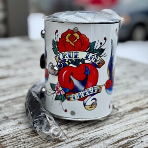 May include: White metal bucket with a black handle and a tattoo-style design. The design features a red rose, a heart, and the words "TRUE LOVE FOREVER" on a banner. The bucket has silver accents.