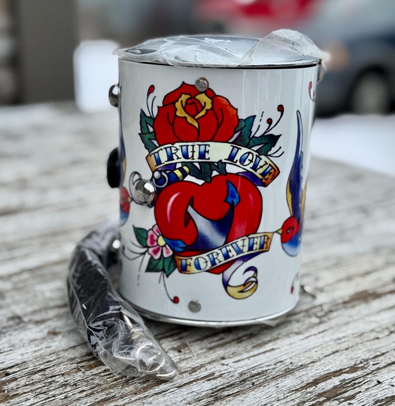 May include: White metal bucket with a black handle and a tattoo-style design. The design features a red rose, a heart, and the words "TRUE LOVE FOREVER" on a banner. The bucket has silver accents.
