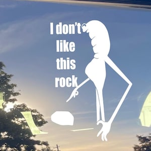 May include: White vinyl decal with the text "I don't like this rock" and a cartoon figure pointing at a small rock. The background is a blue sky with some trees.