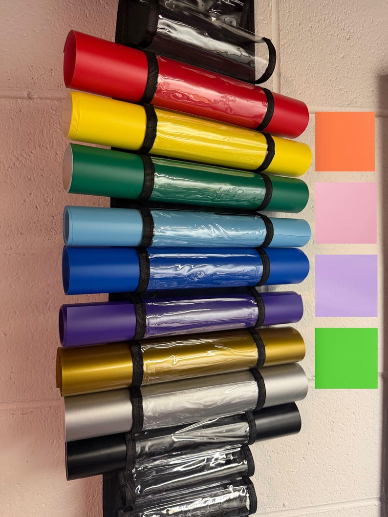Puede incluir: Una colecci&oacute;n de l&aacute;minas de vinilo enrolladas en varios colores, incluyendo rojo, amarillo, verde, azul, morado, dorado, plateado y negro. Cada rollo est&aacute; asegurado con una correa negra y almacenado en un soporte de pl&aacute;stico transparente. Se ven muestras de color.