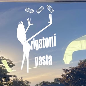 May include: White decal of a figure juggling rigatoni pasta. The figure has long arms and legs, with the words "rigatoni pasta" in bold, white letters below. The background is a blue sky with some trees.