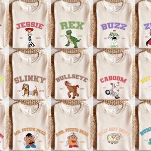 May include: A selection of beige t-shirts, each showcasing a different character from a well-known animated film. The shirts feature character names in a varsity style, accompanied by an image and the year 1995 or 2019.