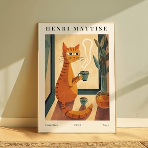 Op de afbeelding: Een ingelijste kunstprint met een gestileerde oranje kat die een kop koffie vasthoudt, met stoom die opstijgt. De print is gelabeld "HENRI MATISSE" en bevat de tekst "Collection 1953 No.1".