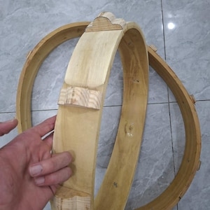 Könnte beinhalten: Zwei unfertige Holzreifen, einer wird von einer Hand gehalten, mit dekorativen Schnitzereien. Das Holz hat eine helle, natürliche Farbe. Die Reifen scheinen Teil eines größeren Bastelprojekts oder Dekorationsgegenstands zu sein.