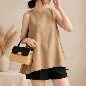 May include: A sleeveless tan linen top paired with black shorts. A black and woven straw handbag with a gold clasp is held in the hand. The outfit is simple and elegant, suitable for warm weather.