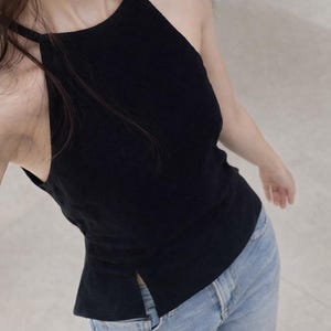Könnte beinhalten: Ein schwarzes Neckholder-Top mit hohem Ausschnitt und geschlitztem Saum. Dazu wird eine hellblaue Jeans getragen. Das Top hat dünne Träger und eine figurbetonte Silhouette, geeignet für Freizeitkleidung.