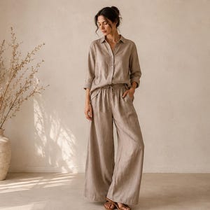 Op de afbeelding: Een beige tweedelige set bestaande uit een overhemd met lange mouwen, knoopsluiting en kraag, en een bijpassende broek met wijde pijpen en een trekkoord in de taille. De outfit is gemaakt van gestructureerde stof en heeft een losse pasvorm.