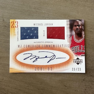 May include: A Michael Jordan commemorative trading card. The card shows Jordan in a Bulls jersey, jersey swatches, and his signature. Text includes "MJ Comeback Commemorative" and "2001-02". The card is numbered 23/23.