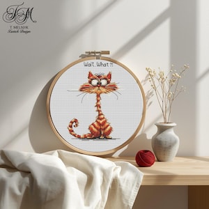 May include: A cross-stitch embroidery hoop featuring a cartoon cat with an elongated neck and surprised expression. The cat is orange and red with the text "Wait. What?!" above it. The hoop is displayed on a wooden surface.