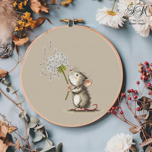 Könnte beinhalten: Kreuzstich-Stickerei einer grauen Maus, die einen Löwenzahn hält. Die Maus befindet sich in der Mitte eines hölzernen Stickrahmens. Der Hintergrund ist ein hellbrauner Stoff. Das Design enthält den Text "T. Melnyk Artistic Design".