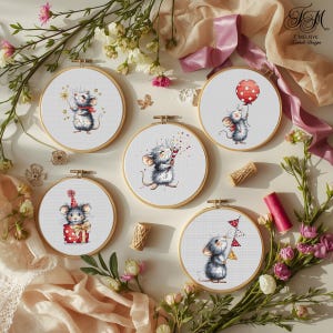 May include: Five cross-stitch embroidery hoops showcasing charming cartoon mice. Each mouse is in a different celebratory pose, holding items such as a sparkler, balloon, party hat, confetti, and pennant flags. The hoops are surrounded by floral arrangements.