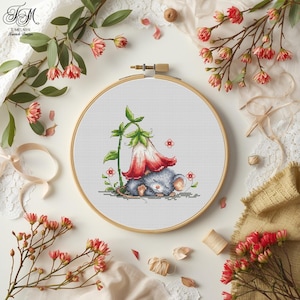 May include: A cross-stitch embroidery hoop featuring a sleeping mouse under a red and white flower. The design includes small red flowers and green leaves. The wooden hoop is set against a white background with floral accents and the text "T. Melnyk, Stitch Design".