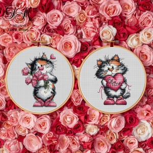 May include: Two cross-stitch embroidery hoops featuring cartoon cats. One cat holds a bouquet of pink roses, the other holds a pink heart with "Be Mine" on it. The background is a bed of pink and red roses.