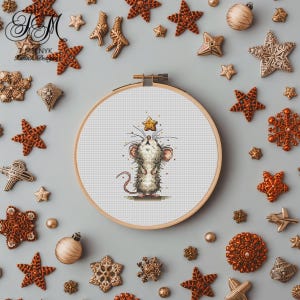 May include: A cross-stitch embroidery hoop featuring a cartoon mouse reaching for a star. The design is surrounded by bronze and gold Christmas ornaments, including stars and baubles, on a gray background. The hoop is held in a wooden frame.