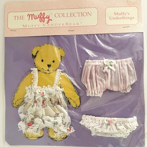 May include: A Muffy VanderBear doll set, featuring a yellow bear cutout and two sets of underthings. One set is white with a floral pattern, and the other two are pink and white striped and white with pink polka dots. The packaging reads "The Muffy Collection".