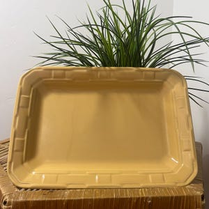 May include: A rectangular yellow ceramic serving tray featuring a raised basket-weave pattern along the wide, flat rim. The center of the tray is smooth and recessed, with a glossy finish that reflects light across its solid, mustard-toned surface.