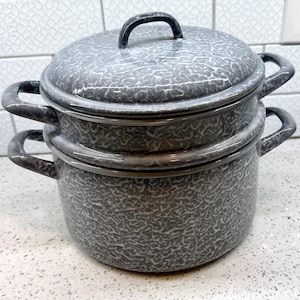 May include: Two-piece gray enamelware cooking pot set with lids and handles. The pots have a speckled pattern and a black rim and handle. The set is designed for cooking and food preparation.