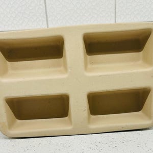 May include: A beige rectangular plastic tray with four recessed compartments. The tray has a slightly curved shape and is designed with angled sides for each compartment. The overall design is simple and functional.