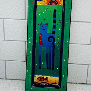 May include: A green ceramic serving tray with a blue cat and a fish design. The cat has a blue body, black stripes, and a red tail. The fish is orange with black spots. The tray is decorated with white and yellow dots.