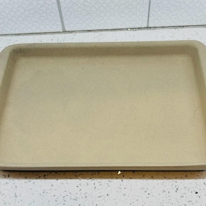 May include: A rectangular, light tan baking stone with rounded corners. The stone has a slightly raised edge and a smooth surface. The baking stone is designed for even heat distribution and is suitable for baking various foods.