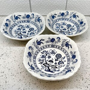 May include: Three white ceramic bowls featuring a scalloped edge and a blue onion pattern. Each bowl displays a central floral motif surrounded by intricate blue botanical designs, including stylized pomegranates and leaves on a white background.
