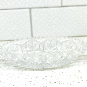 May include: A clear glass bowl with a cut glass design and two handles. The bowl is oval shaped and has a delicate, intricate pattern.