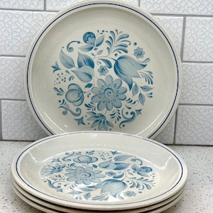 May include: A set of vintage ceramic plates with a floral design. The plates feature a cream-colored base with a blue floral pattern and a blue rim. The set includes both large dinner plates and smaller plates.