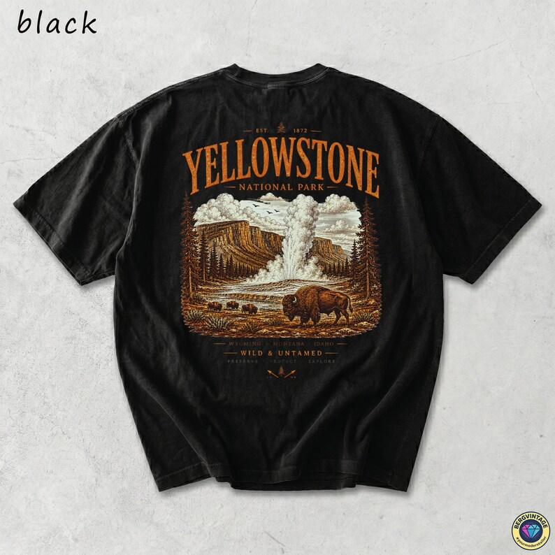 May include: Black t-shirt featuring a Yellowstone National Park graphic. The design includes a bison, geyser, and mountain landscape in shades of brown, orange, and white. The text "Yellowstone National Park" is arched across the top.