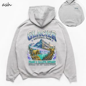 Op de afbeelding: Een asgrijze hoodie met een grote graphic op de achterkant van Glacier National Park met een beer, een berggeit, bergen en een waterval. De tekst luidt Glacier National Park, Peaks & Valleys, Untamed, Montana, Est. 1910, Glacial Summits.